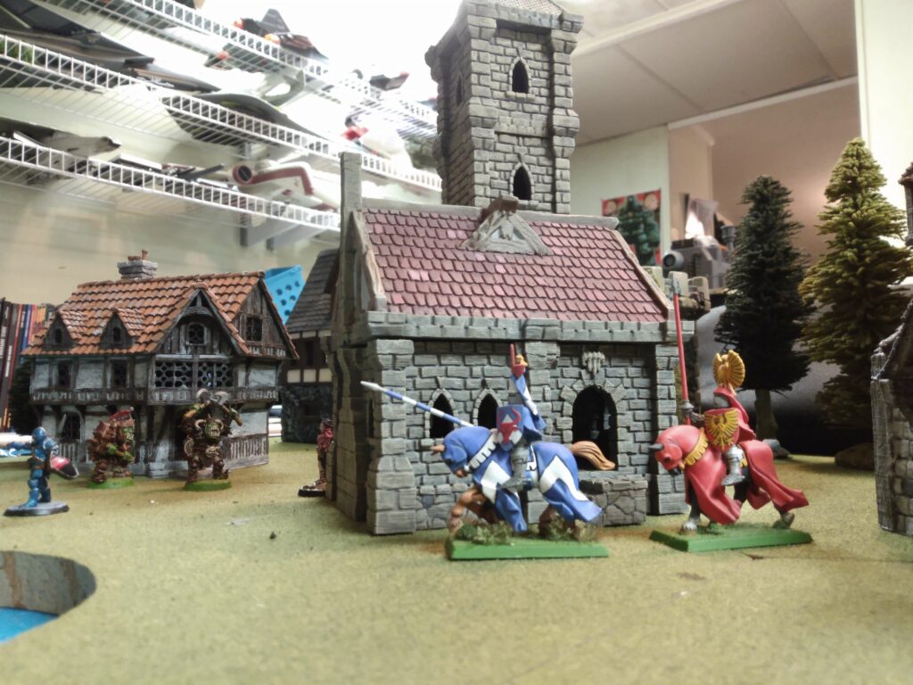 Mounted knights ride by a miniature stone chapel building in 28mm wargame scale. 3D printed with FDM.