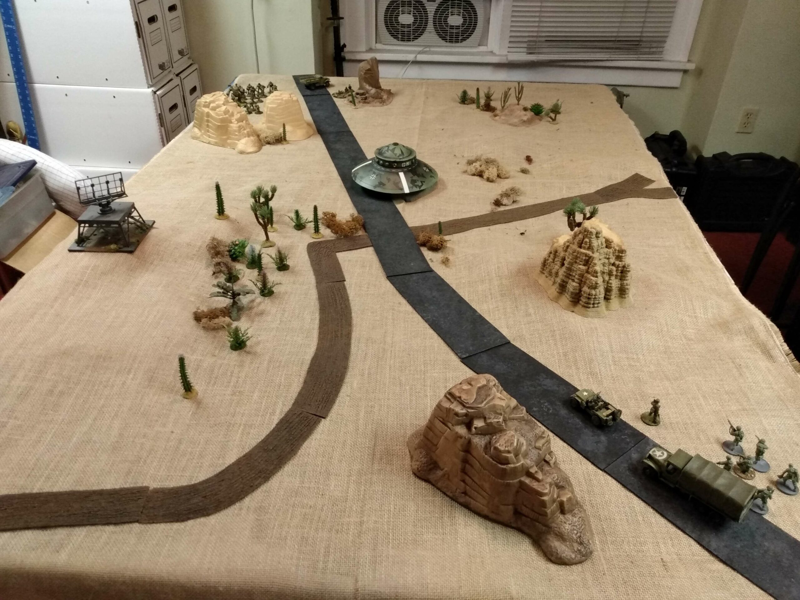 WW2 desert wargaming table with a UFO in the center and army troops surrounding it.
