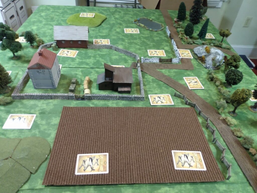 Miniature wargame tabletop layout of a farm and crossroads.