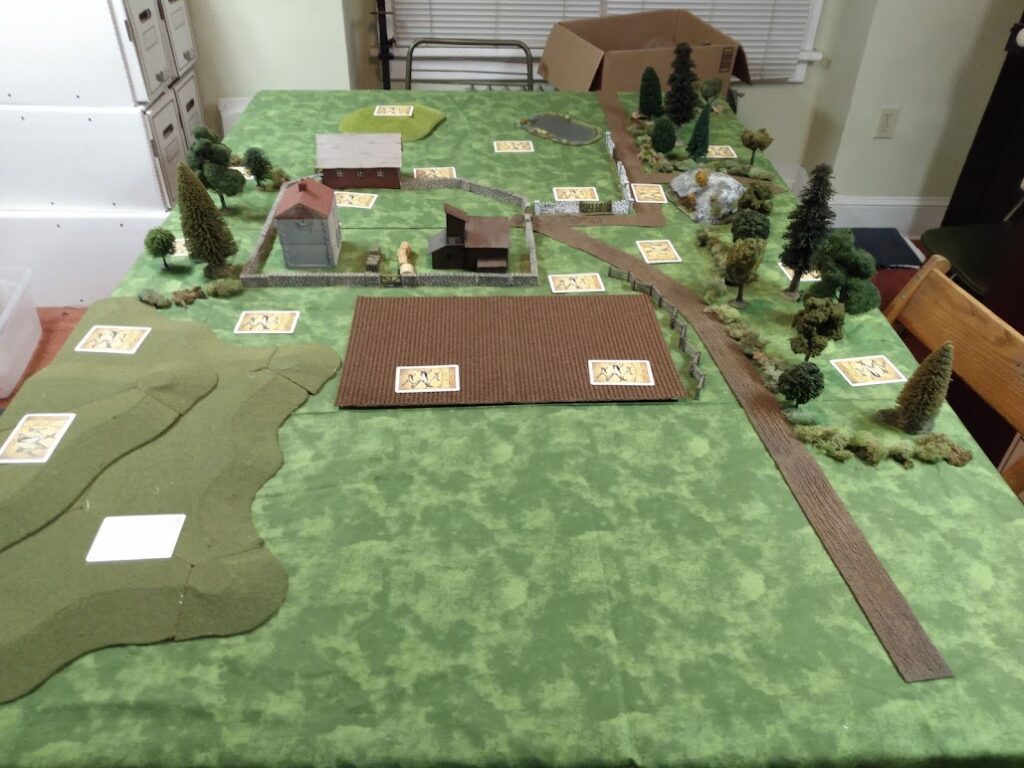 Miniature wargame tabletop layout of a farm and crossroads.