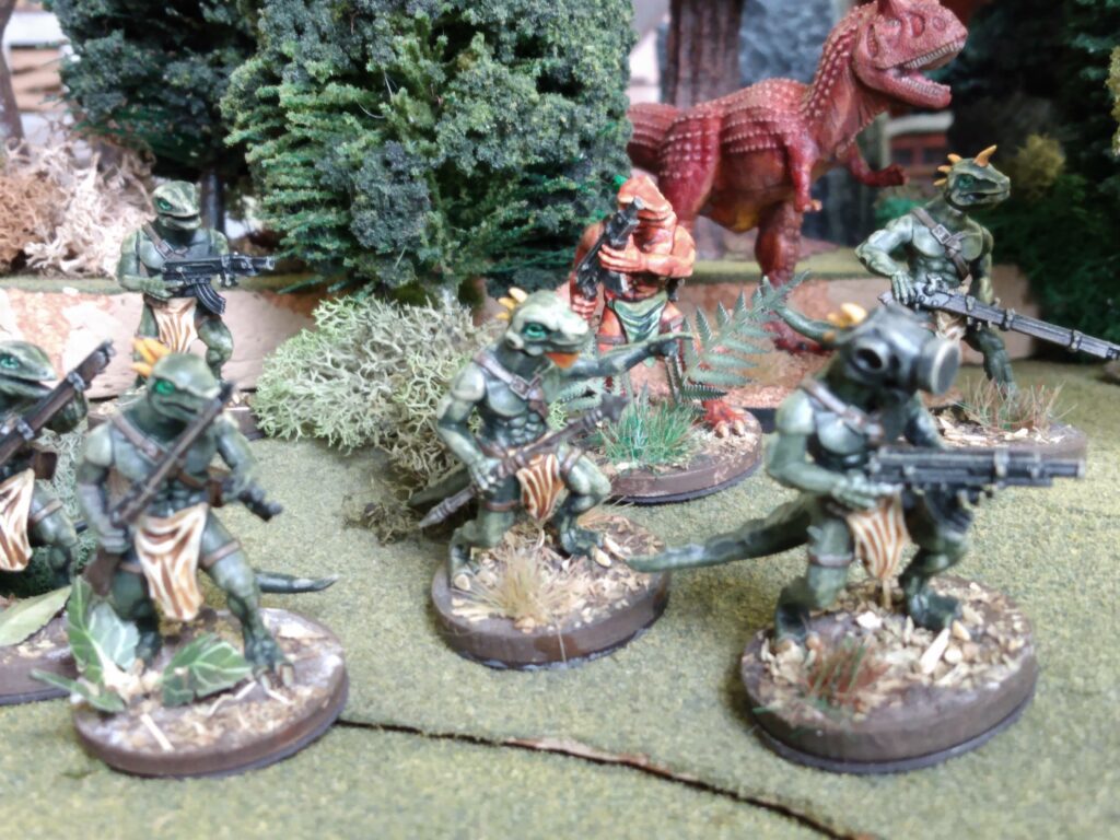 Wargames Atlantic Lizardman with rifles and a Reaper Carnotaurus miniature advance out of a forest of the Hollow Earth