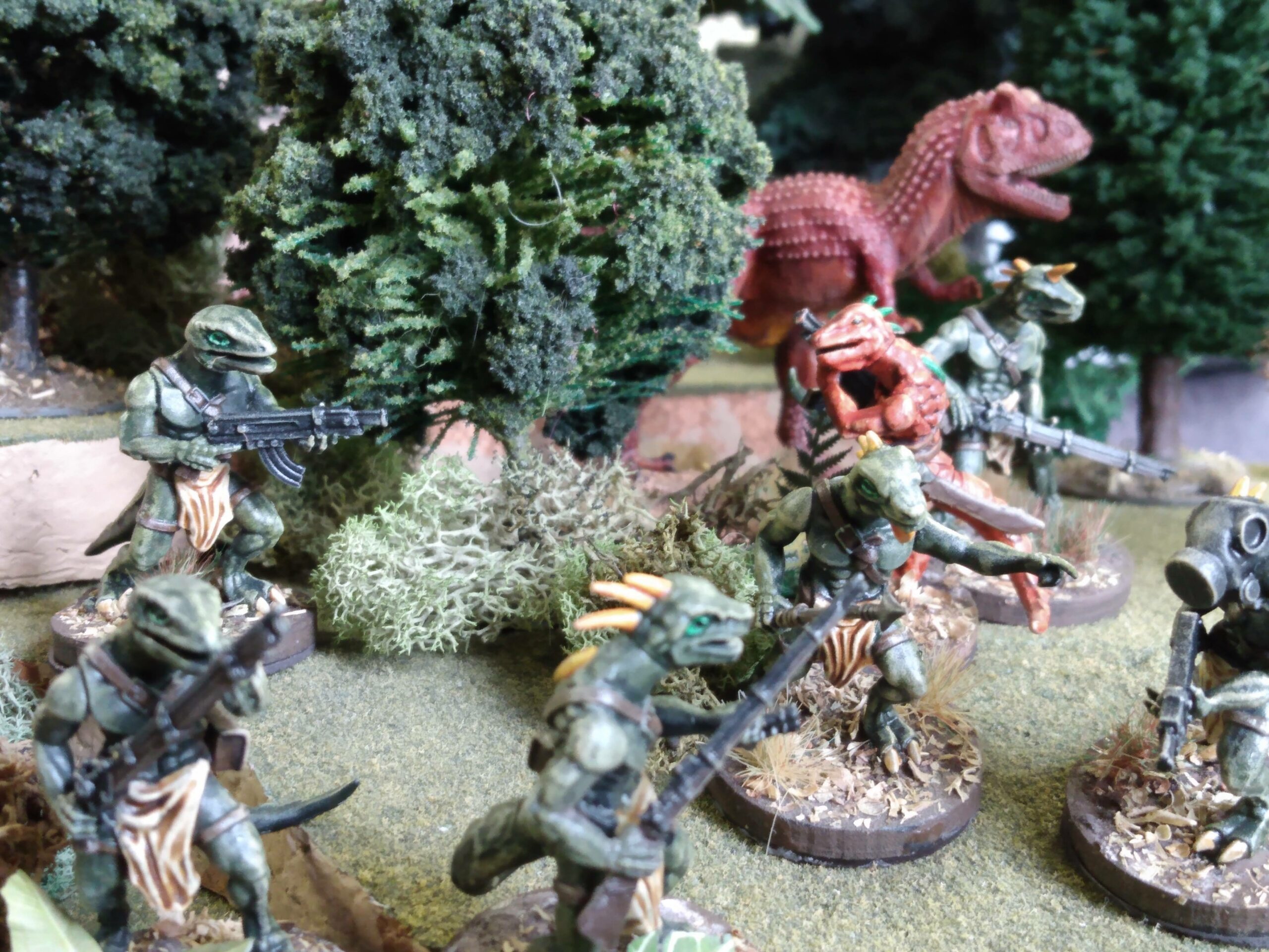 Wargames Atlantic Lizardman with rifles and a Reaper Carnotaurus miniature advance out of a forest of the Hollow Earth
